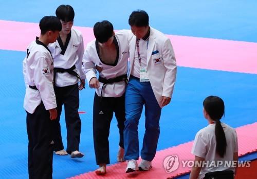 South Korean taekwondo practitioner Kim Seon-ho (C) is assisted by his coach to leave the mat after finishing the first set of the men's team poomsae final at the 18th Asian Games in Jakarta on Aug. 19, 2018. (Yonhap)