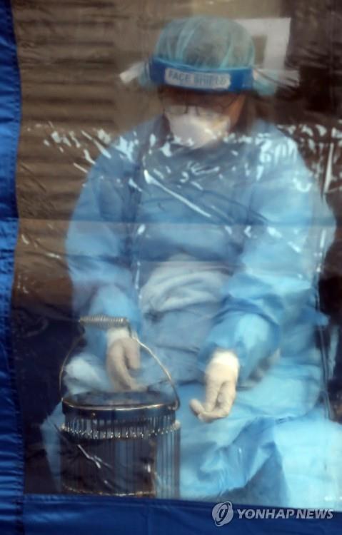 A medical worker warms himself at a stove as he prepares to conduct coronavirus tests at a makeshift clinic at the National Medical Center in Seoul on Dec. 17, 2020 (Yonhap)