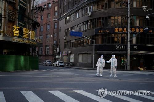 This Reuters photo shows workers in protective suits keeping watch on a street during a lockdown amid the COVID-19 pandemic in Shanghai, in this file photo taken April 16, 2022. (PHOTO NOT FOR SALE) (Yonhap)