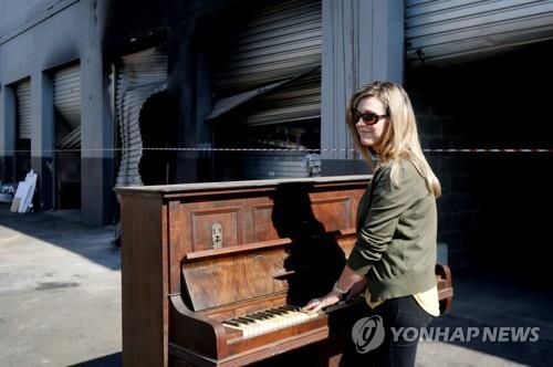 18일 소셜미디어에서 공연으로 화제가 된 제니 보우스가 약탈된 창고 앞에서 피아노를 치고 있다. [로이터=연합뉴스]