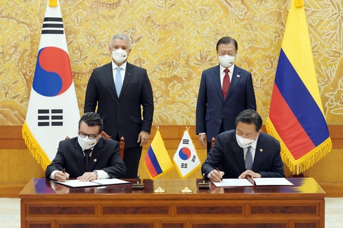 El presidente surcoreano, Moon Jae-in (dcha., de pie), y el presidente colombiano, Iván Duque Márquez (izda., de pie), observan al ministro de los Asuntos de Patriotas y Veteranos, Hwang Ki-chul (dcha.), y el embajador de Colombia ante Seúl, Juan Carlos Caiza Rosero, quienes firman un MOU sobre la cooperación en asuntos de veteranos, el 25 de agosto de 2021, en la oficina presidencial, Cheong Wa Dae, en Seúl, tras una reunión cumbre entre los líderes de ambos países.