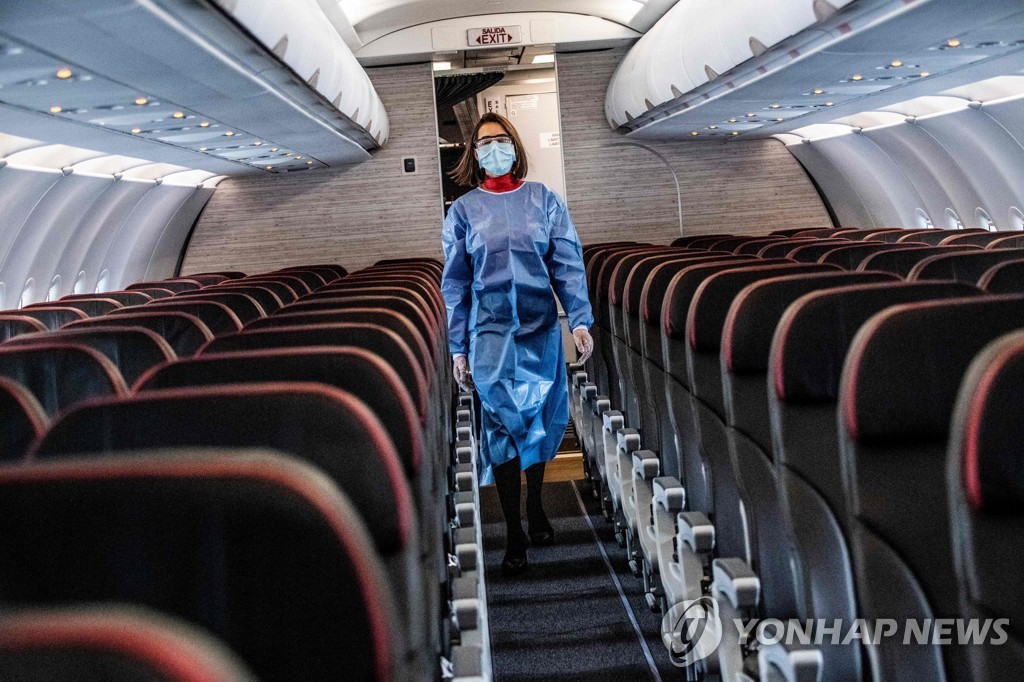 한 비행기 승무원이 마스크와 방호복을 착용한 채 기내를 점검하고 있다.[AFP=연합뉴스 자료사진]