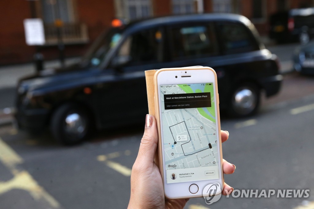 스마트폰으로 우버 서비스를 이용하는 여성 앞에 런던의 블랙캡 택시가 지나가는 모습 [AFP=연합뉴스]