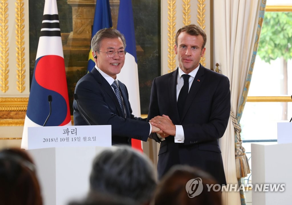 South Korean President Moon Jae-in (L) and French President Emmanuel Macron clasp hands after holding a joint press conference to announce the outcome of their bilateral summit held at the Elysee Palace in Paris on Oct. 15, 2018. (Yonhap)