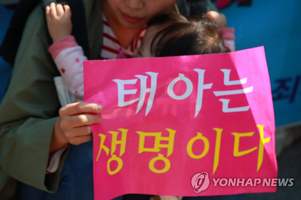 A woman with a baby holds a sign that reads "A fetus is a life," during an anti-abortion rally held in Seoul ahead of the Constitutional Court's ruling on April 11, 2019. (Yonhap)