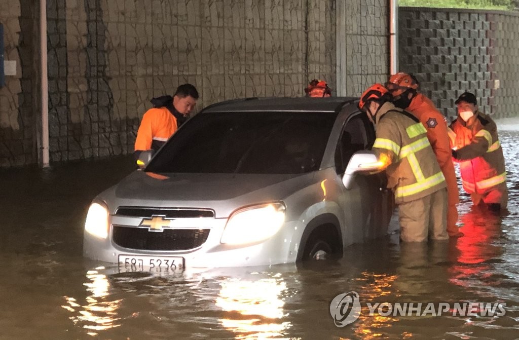 Firefighters help a driver on a flooded road in Incheon, west of Seoul, on July 23, 2020, in this photo provided by the Incheon Metropolitan Fire and Disaster Headquarters, as heavy rains pounded most of the country. (PHOTO NOT FOR SALE) (Yonhap)