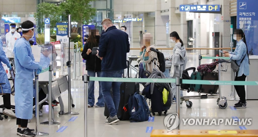 International arrivals show their passports to officials wearing protective gear at Incheon International Airport, South Korea's main gateway west of Seoul, on Oct. 22, 2020. (Yonhap)