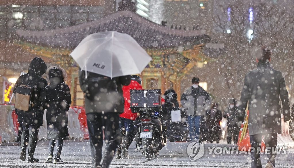 Citizens walk on a snow-covered street in Seoul on Jan. 6, 2021, as the weather agency issued heavy snow alerts for the capital and other parts of the country. (Yonhap)