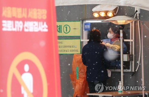 A health worker collects a sample from a citizen at a makeshift COVID-19 testing facility amid snowfall in Seoul on Jan. 18, 2021. (Yonhap)