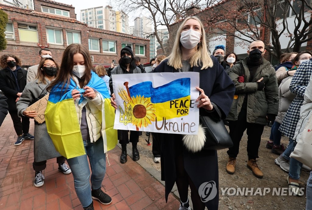Ukrainians living in South Korea hold up Ukraine's national flag and a painting depicting their aspirations for peace for their home country at a Catholic church in western Seoul on Feb. 26, 2022, as Russia has intensified its attack on Ukraine. (Yonhap)