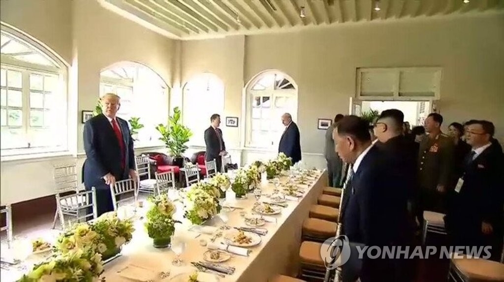 In this photo captured from the homepage of The Straits Times, U.S. President Donald Trump and North Korean leader Kim Jong-un attend a working lunch following their historic summit at the Capella Hotel on the Singaporean resort island of Sentosa on June 12, 2018. (Yonhap)