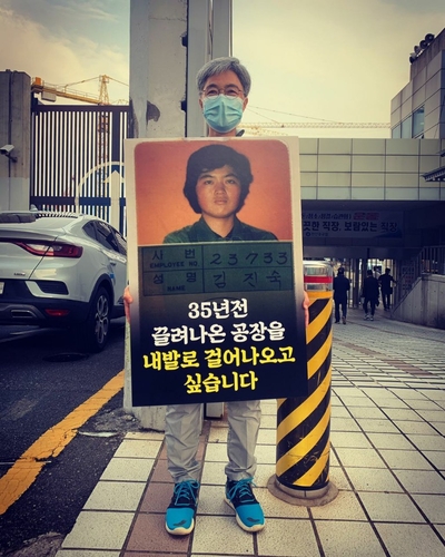 Kim Jin-suk, 60, holds a picket that reads, "I want to walk out of the shipyard where I was forcibly dragged out 35 years ago on my own feet," at the main gate of Hanjin Heavy Industries & Construction Co. in Busan, in this photo provided by her. (PHOTO NOT FOR SALE) (Yonhap)