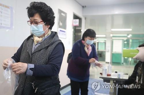 People wear disposable gloves before casting their ballots to protect themselves against the coronavirus at a polling station in the southern port city of Busan on April 7, 2021 (Yonhap) 
