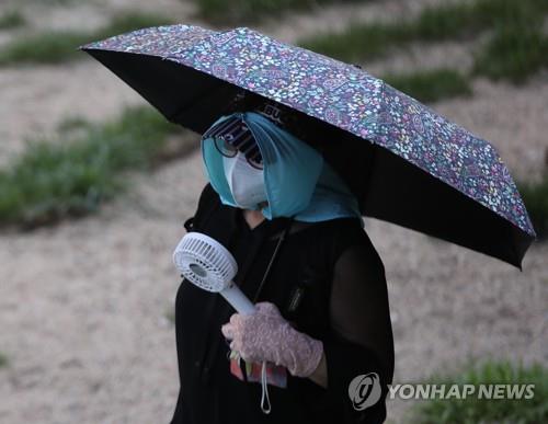 A woman walks along Hongje Stream in Seoul, covering herself from the burning sun while holding a parasol and a fan on July 21, 2021. (Yonhap)