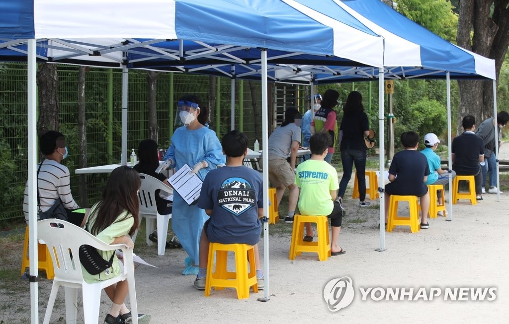 En la imagen, tomada el 20 de junio de 2020, se muestra a los estudiantes de sexto grado de primaria y al personal de la Escuela Primaria Oksu esperando para realizarse la prueba del coronavirus en un centro de examen temporal, instalado en el gimnasio de la escuela, en Seúl.