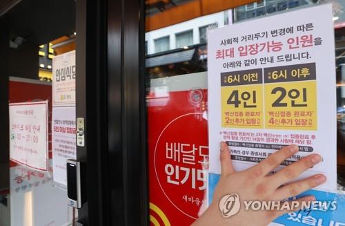 La foto, tomada el 17 de octubre de 2021, muestra a un trabajador pegando un aviso sobre las normas de distanciamiento social revisadas en la ventana de un restaurante de Seúl.