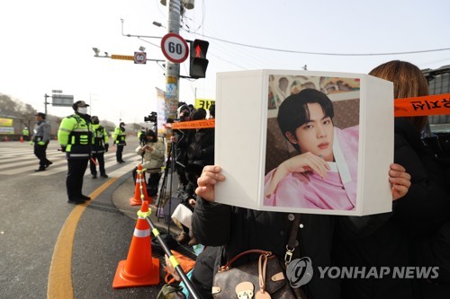 Una fan de Jin, integrante de la sensación del K-pop BTS, sostiene una foto del cantante frente a un campo de entrenamiento de una división de primera línea del Ejército en Yeoncheon, a 60 kilómetros al norte de Seúl, el 13 de diciembre de 2022, donde el miembro de BTS iniciará su servicio militar.