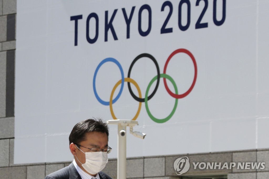 In this Associated Press photo, a man walks past a Tokyo Olympics logo at the Tokyo metropolitan government headquarters building in Tokyo on March 25, 2020. (Yonhap)