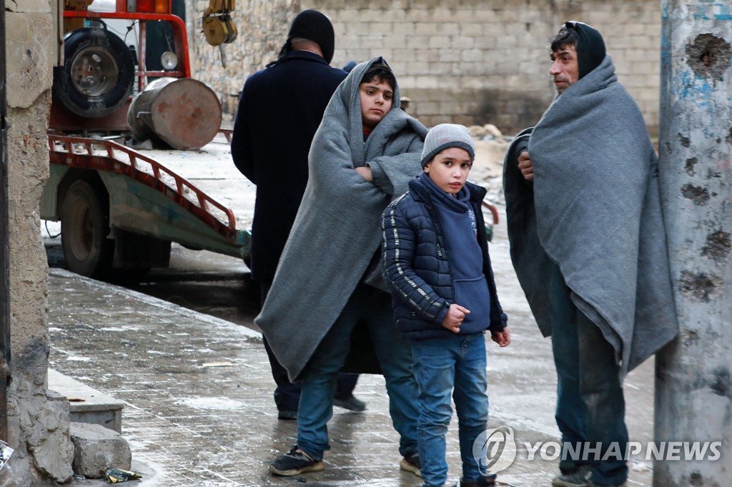 모포를 뒤집어쓰고 거리에 서 있는 시리아 남성과 어린이들