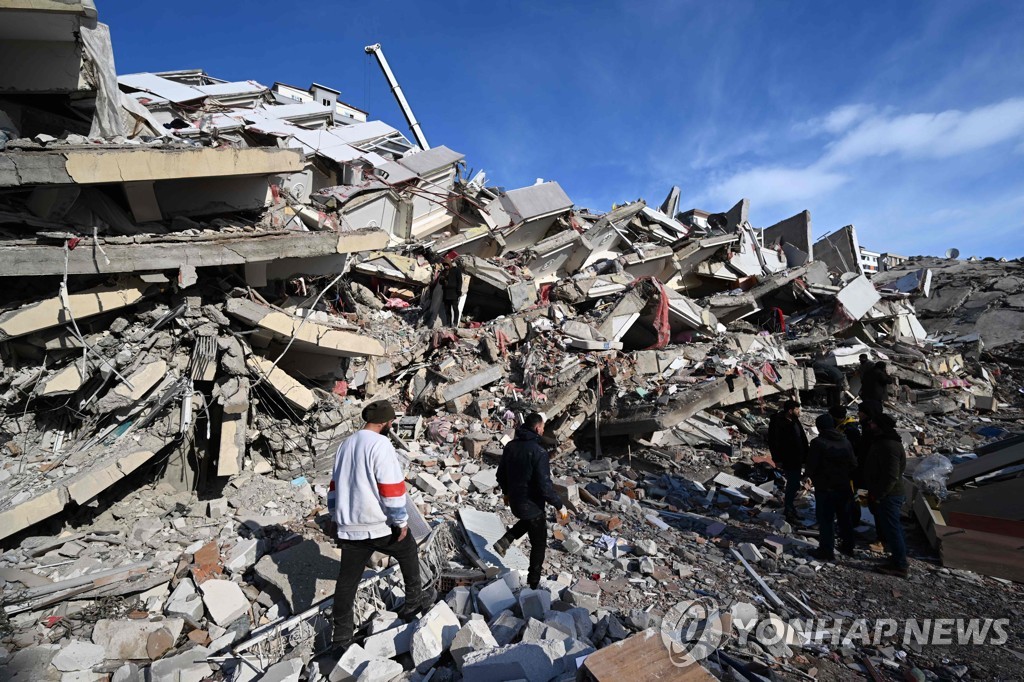 지진 희생자들의 친지들이 방괴된 건물 잔해에서 망연자실한 모습으로 서 있다. [AFP=연합뉴스]