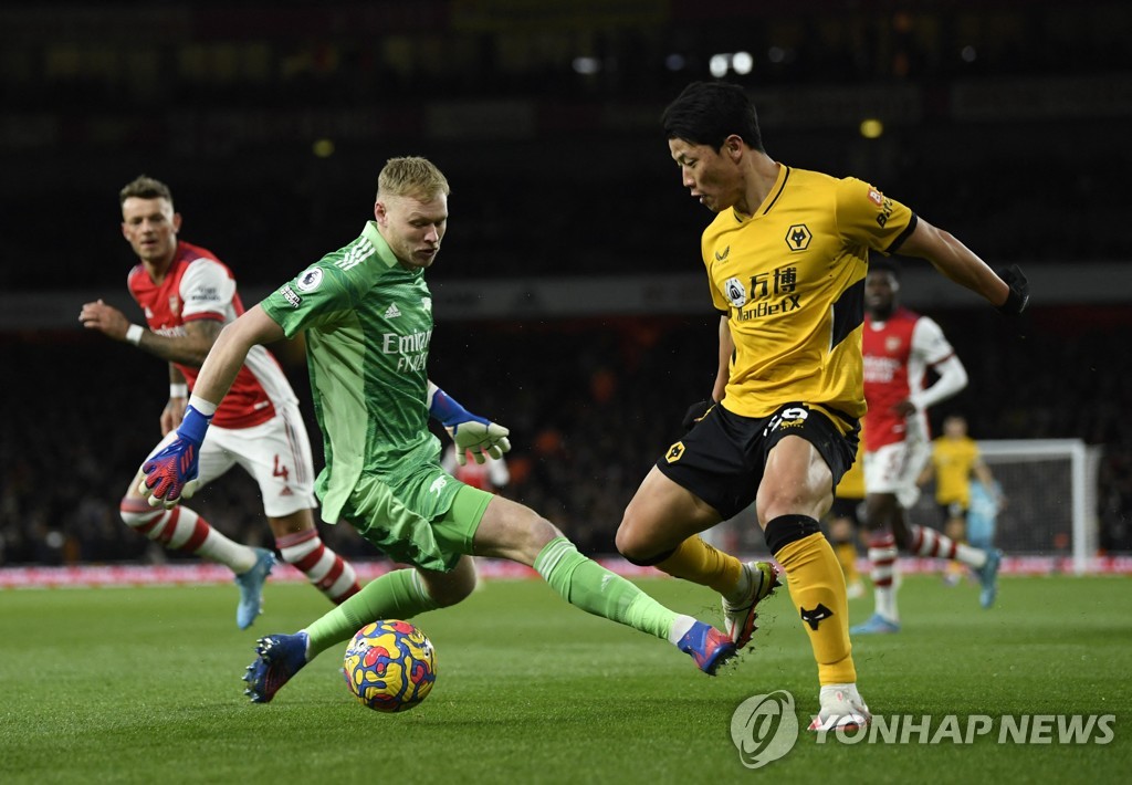 In this Reuters photo, Hwang Hee-chan of Wolverhampton Wanderers (R) scores past Aaron Ramsdale of Arsenal during a Premier League match at Emirates Stadium in London on Feb. 24, 2022. (Yonhap)