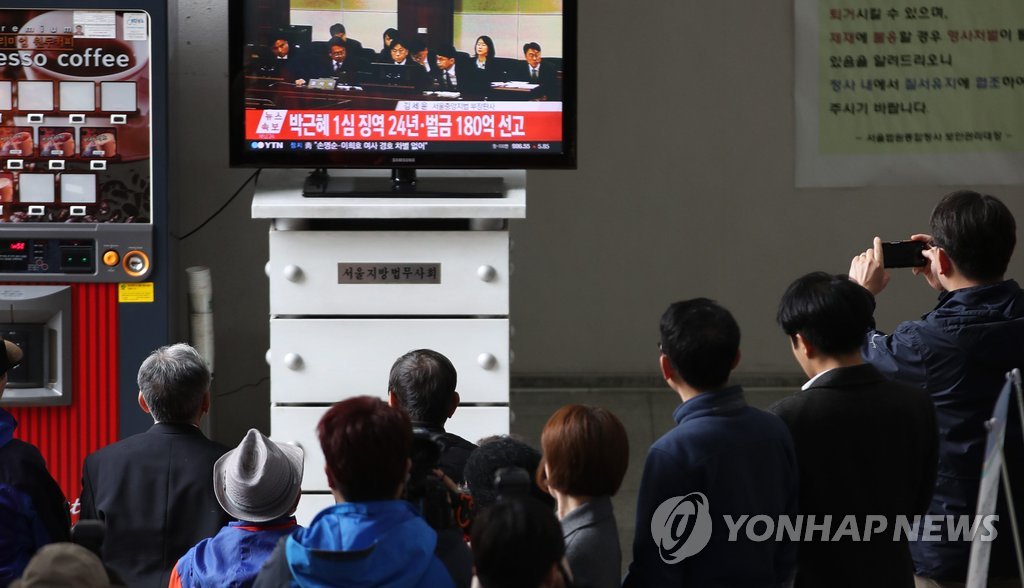 判決公判が開かれたソウル中央地裁に設置されているテレビで生中継を見る市民たち＝６日、ソウル（聯合ニュース）