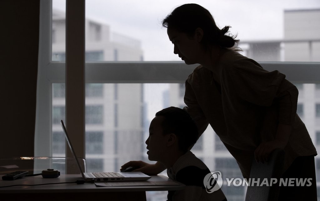 This April 20, 2020 photo shows an elementary school student taking online class with the help of his mother at their home in the central Seoul ward of Yongsan. (Yonhap)