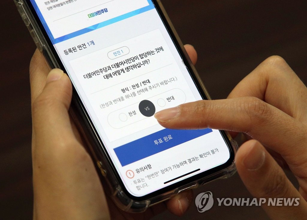 A party member of the ruling Democratic Party casts a ballot on a mobile phone on May 7, 2020, on a bid to merge with its sister party named the Platform Party. (Yonhap)