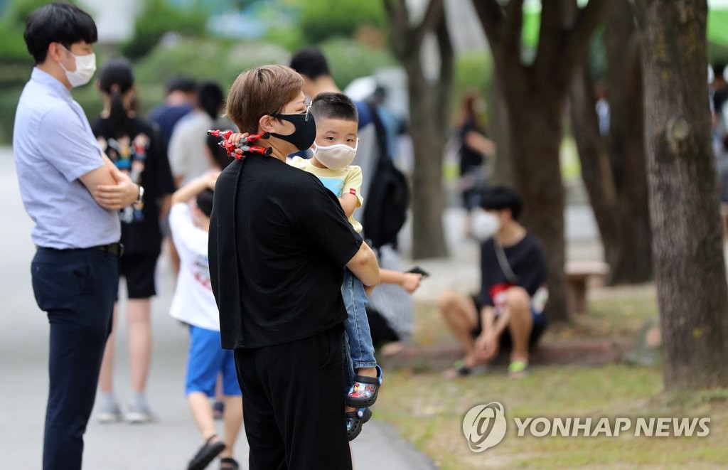 A mother holding her child waits to receive new coronavirus tests at an elementary school in Hwasun, 343 kilometers south of Seoul, on Aug. 24, 2020. (Yonhap)