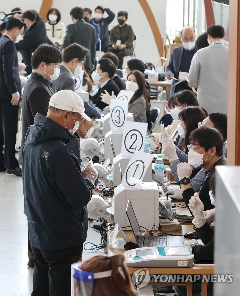 Voters receive ballots at a polling station in Seoul on April 2, 2021, the first day of two-day early voting for the April 7 Seoul mayoral by-election. (Yonhap)