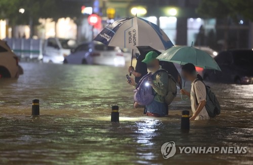 ８日夜、ソウル市江南区の大峙駅付近で冠水した道路を歩く市民たち＝（聯合ニュース）