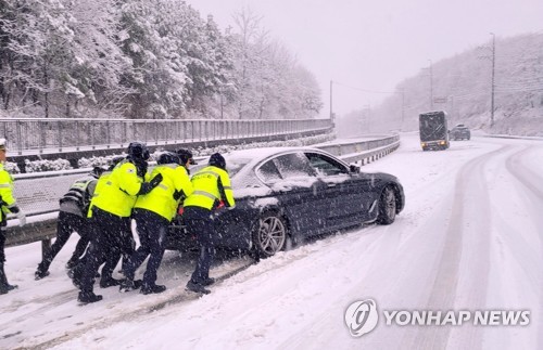 This photo provided by the Gangwon Provincial Police Agency shows police personnel pushing a car on a snow-covered road in the county of Yangyang on Jan. 15, 2023. (PHOTO NOT FOR SALE) (Yonhap)